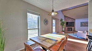 A dining area with a wooden table and leather chairs, a hanging light fixture, and a brick fireplace in the background. - Modern Fayetteville Home < 1 Mi to U of A! (Fayetteville)