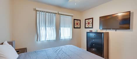 A bedroom with a bed, a dresser, a ceiling fan, and two windows with curtains.