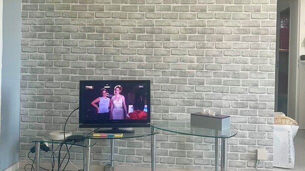 A living room with a brick-patterned wall, a glass coffee table, and a television on a stand. - A bright and sunny one-bedroom apartment with a private terrace and a beautiful, unobstructed view. (Aix-en-Provence)