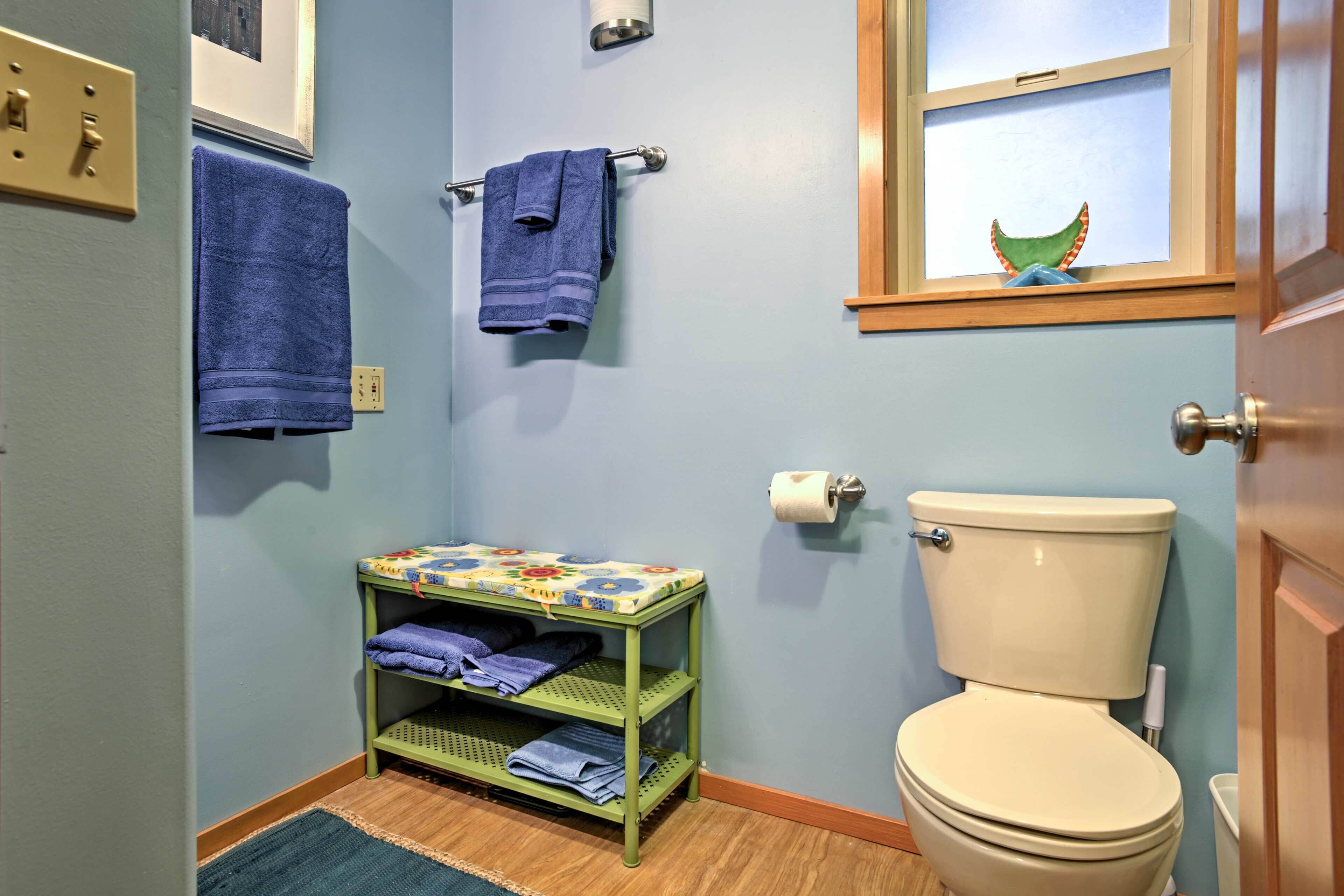 Un bagno con il water, uno scaffale con asciugamani piegati, una cartuccia di carta igienica e una finestra con un oggetto decorativo.