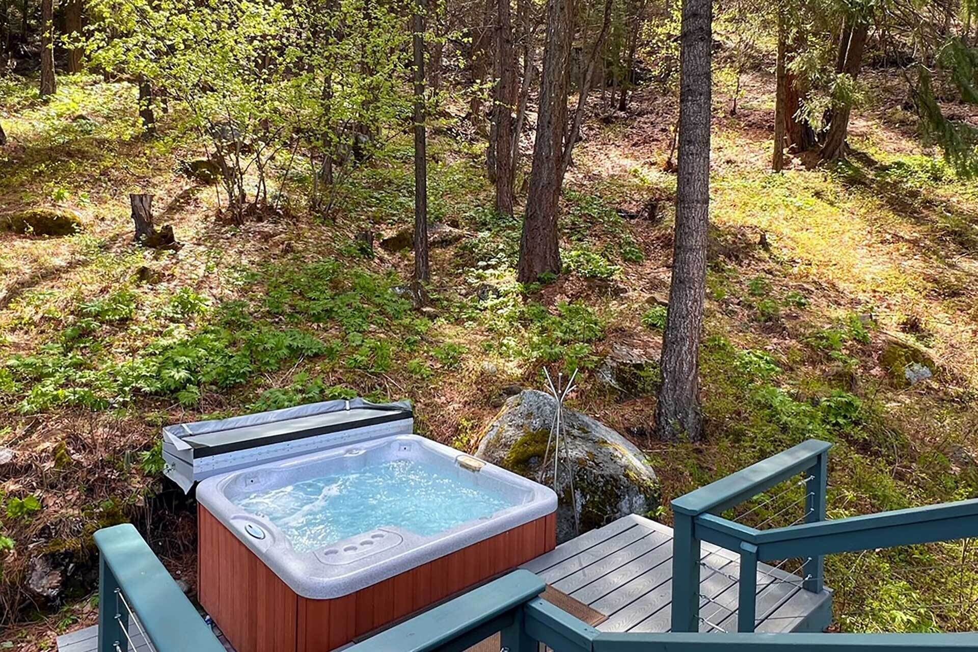 A hot tub in a forested area with a wooden deck and railing.