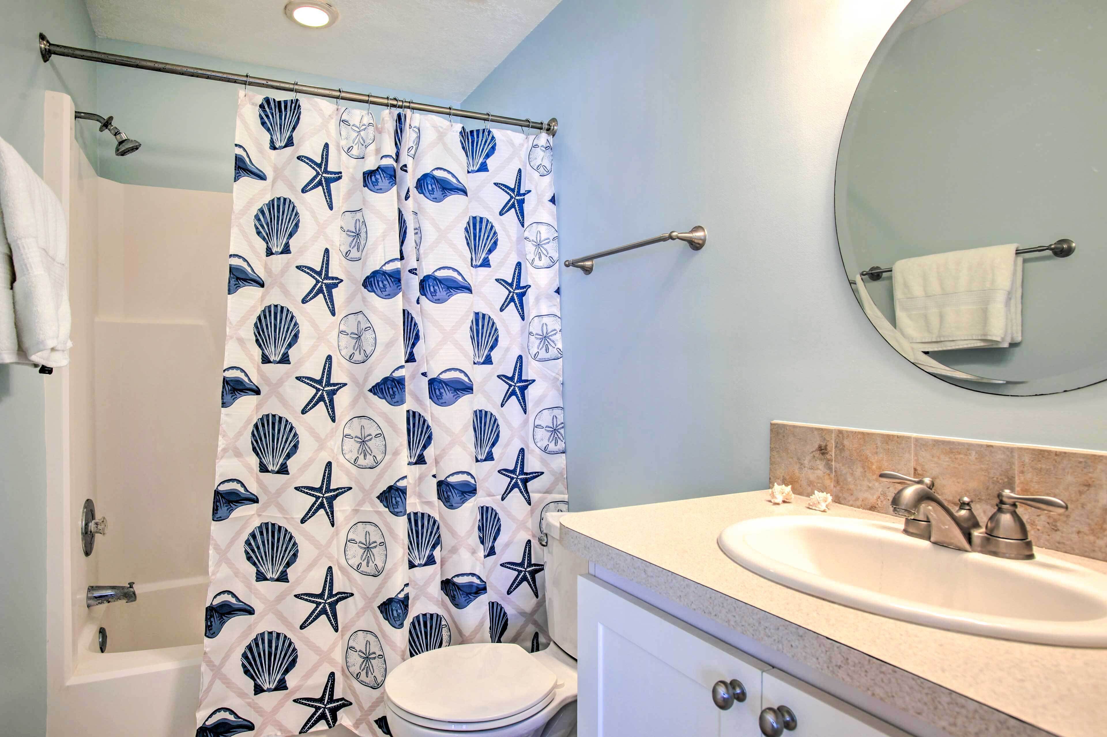 A bathroom with a shower curtain featuring a sea shell and starfish pattern, a white toilet, a sink with a mirror above it, and a towel rack with a towel.
