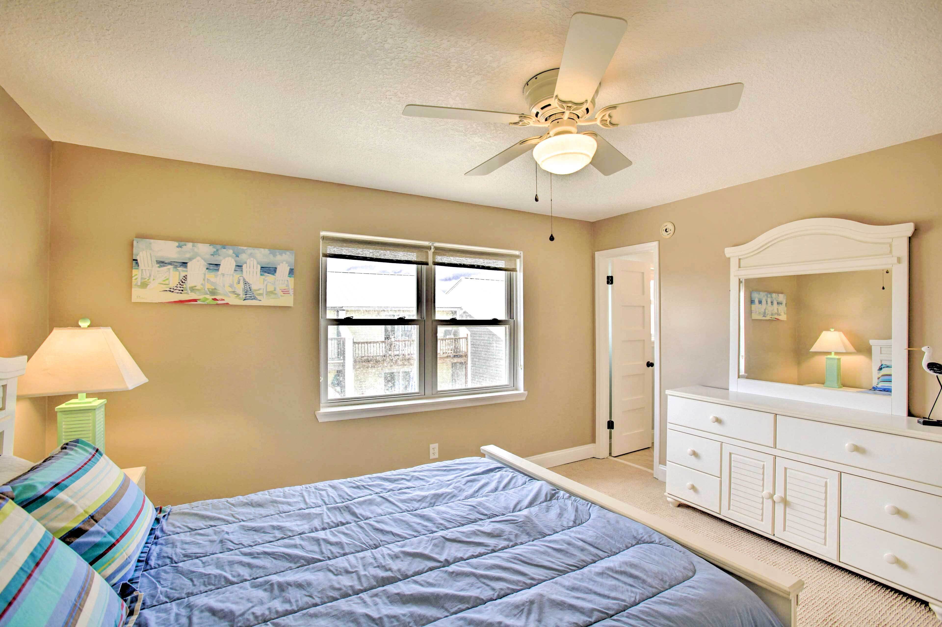 A bedroom with a bed, a dresser, a ceiling fan, a window, and a painting on the wall.