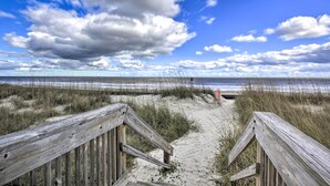 Een houten looppad dat naar een strand leidt, met een heldere lucht en wolken.