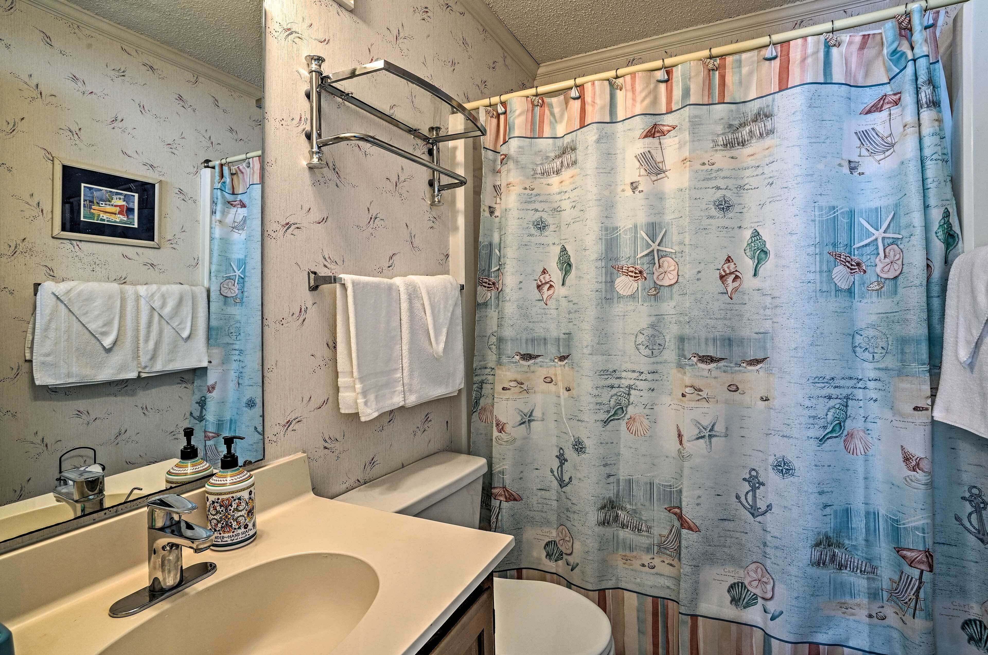 A bathroom with a shower curtain featuring nautical designs, a sink with soap dispensers, and a towel rack with white towels.