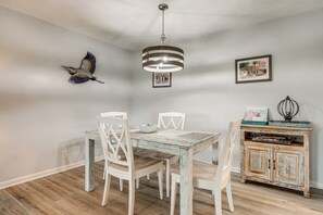 En matplats med ett rustikt träbord, vita stolar, en hängande lampa och en fågelskulptur som sitter fast på väggen.