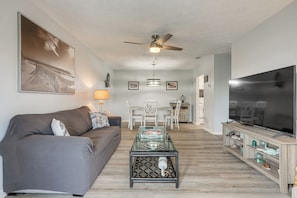 A living room with a sofa, coffee table, TV, and ceiling fan. - < Half-mi to Fort Clinch Beach! Condo w/ Balcony (Fernandina Beach)