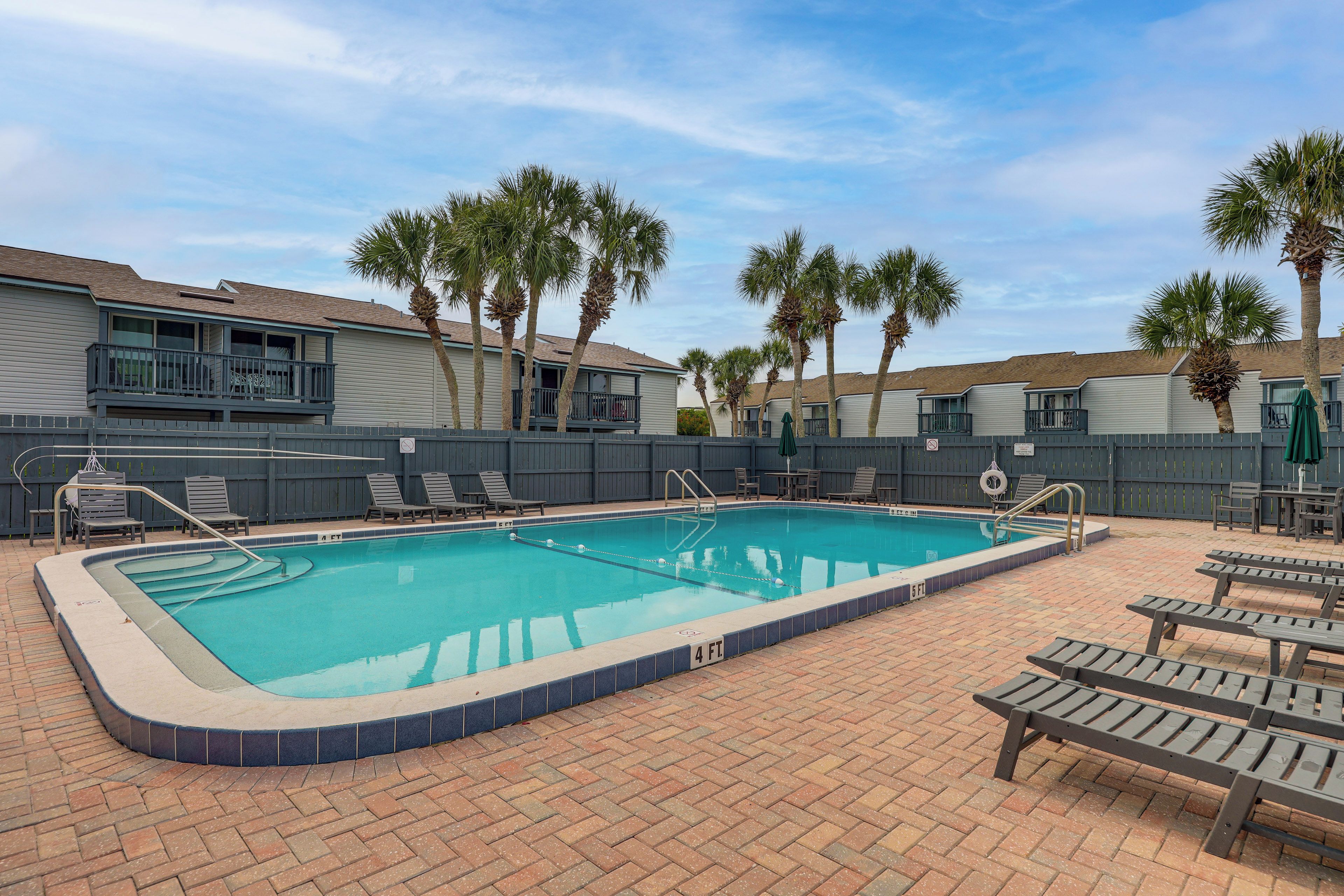 A rectangular swimming pool with a tiled edge, surrounded by lounge chairs and a brick patio.