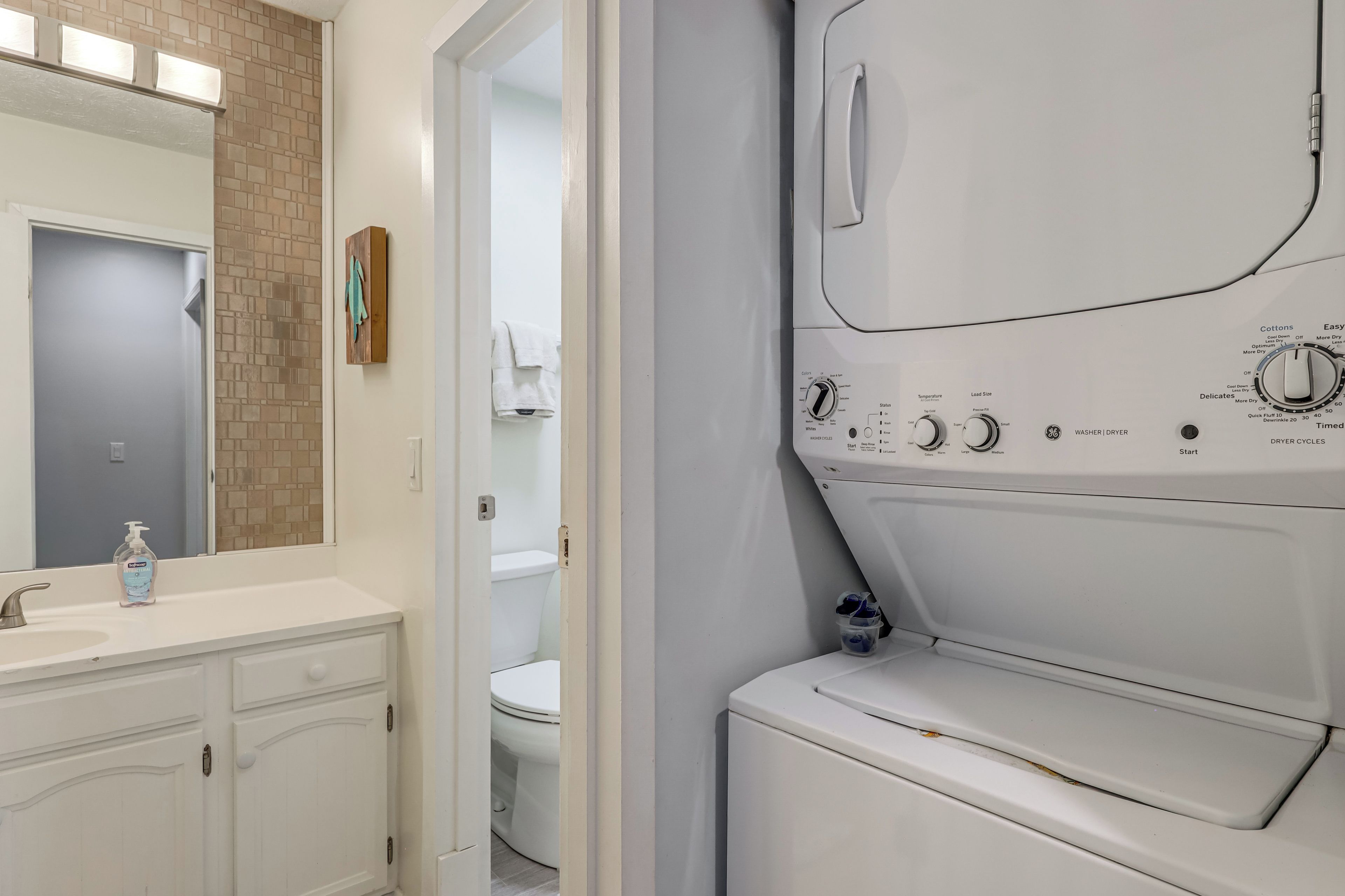 A laundry room with a white dryer, a sink with a soap dispenser, and a toilet visible through an open door.