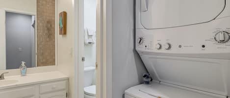 A laundry room with a white dryer, a sink with a soap dispenser, and a toilet visible through an open door.