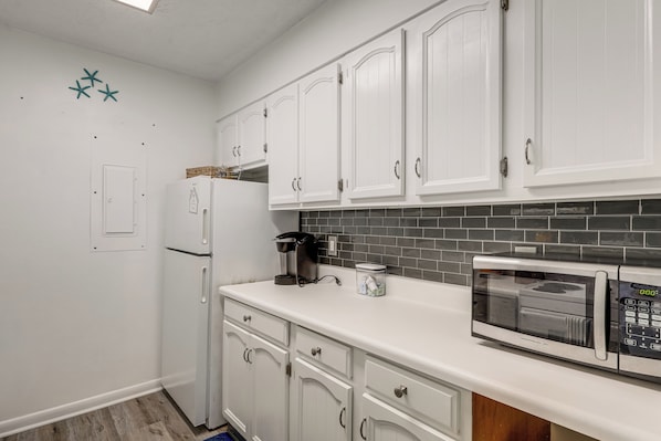 A kitchen with white cabinets, a refrigerator, a coffee maker, a microwave, and a tiled backsplash.