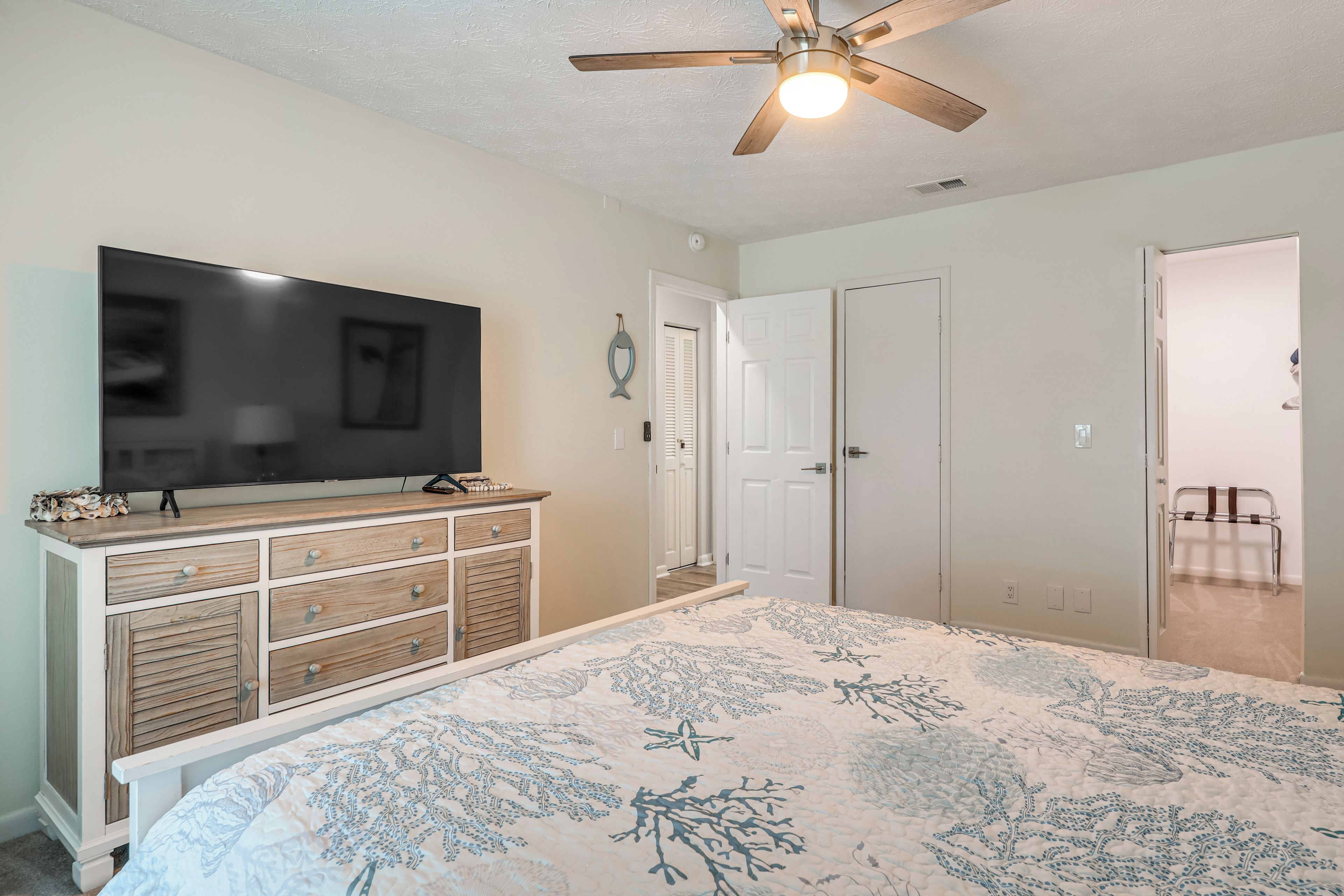 A bedroom with a bed, a TV on a dresser, a ceiling fan, and a door.
