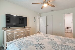 A bedroom with a bed, a TV on a dresser, a ceiling fan, and a door.