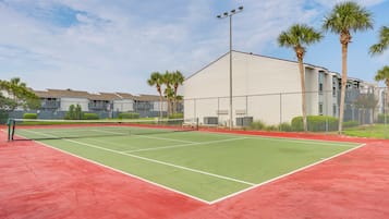 Een tennisbaan met net, omringd door een gaashek en palmbomen op de achtergrond.