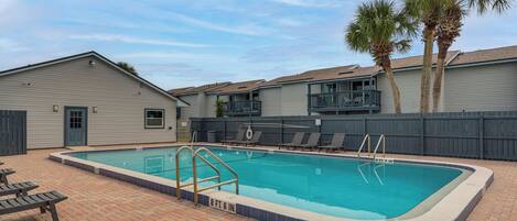 A rectangular swimming pool with a blue border, surrounded by a brick patio.