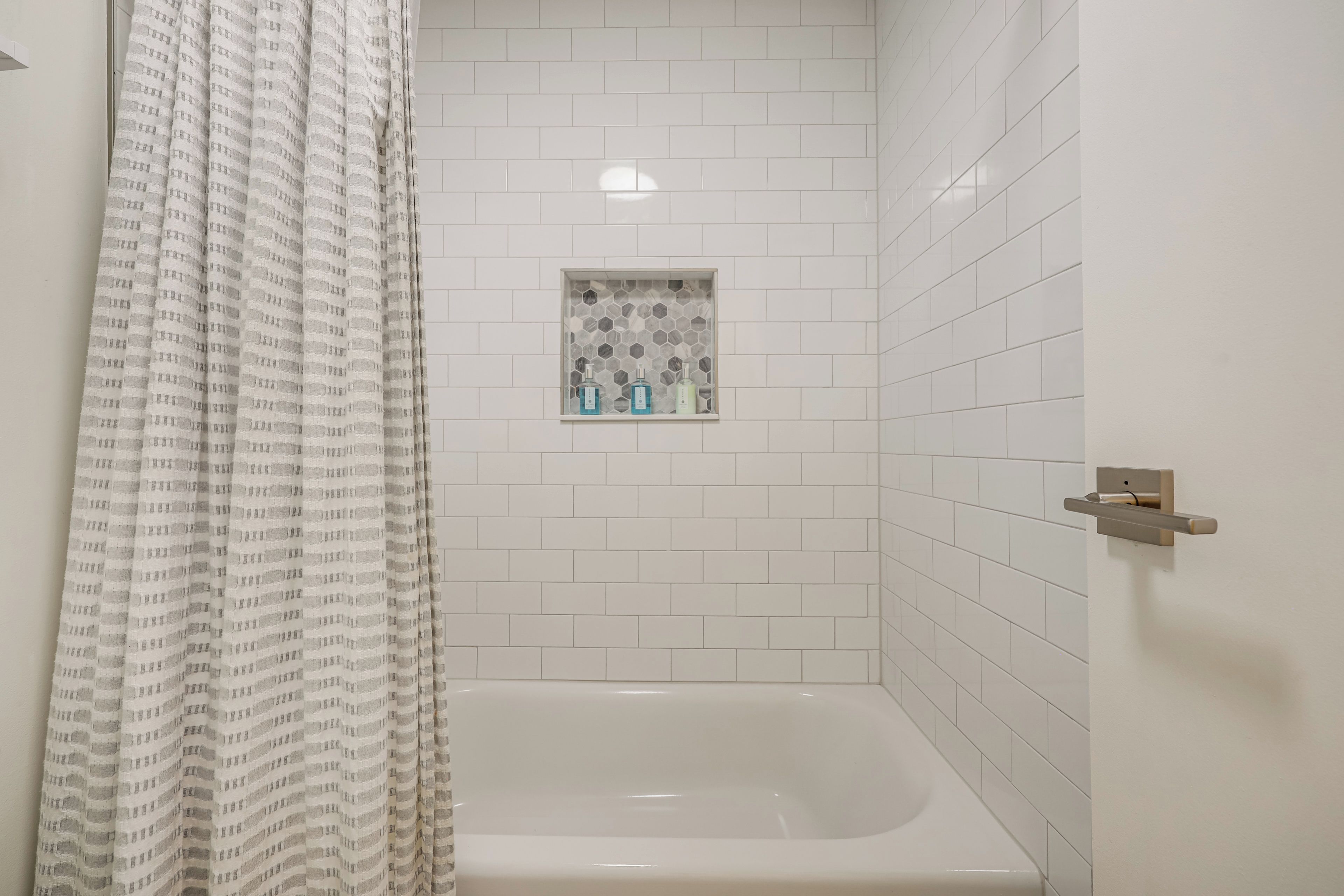 A bathroom with a white bathtub, a shower curtain, and a small shelf with toiletries.