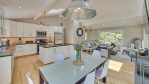 A modern kitchen with white cabinets, a central island, and a dining area with a glass table and white chairs.