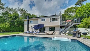 A two-story house with a swimming pool, outdoor furniture, and a barbecue grill.