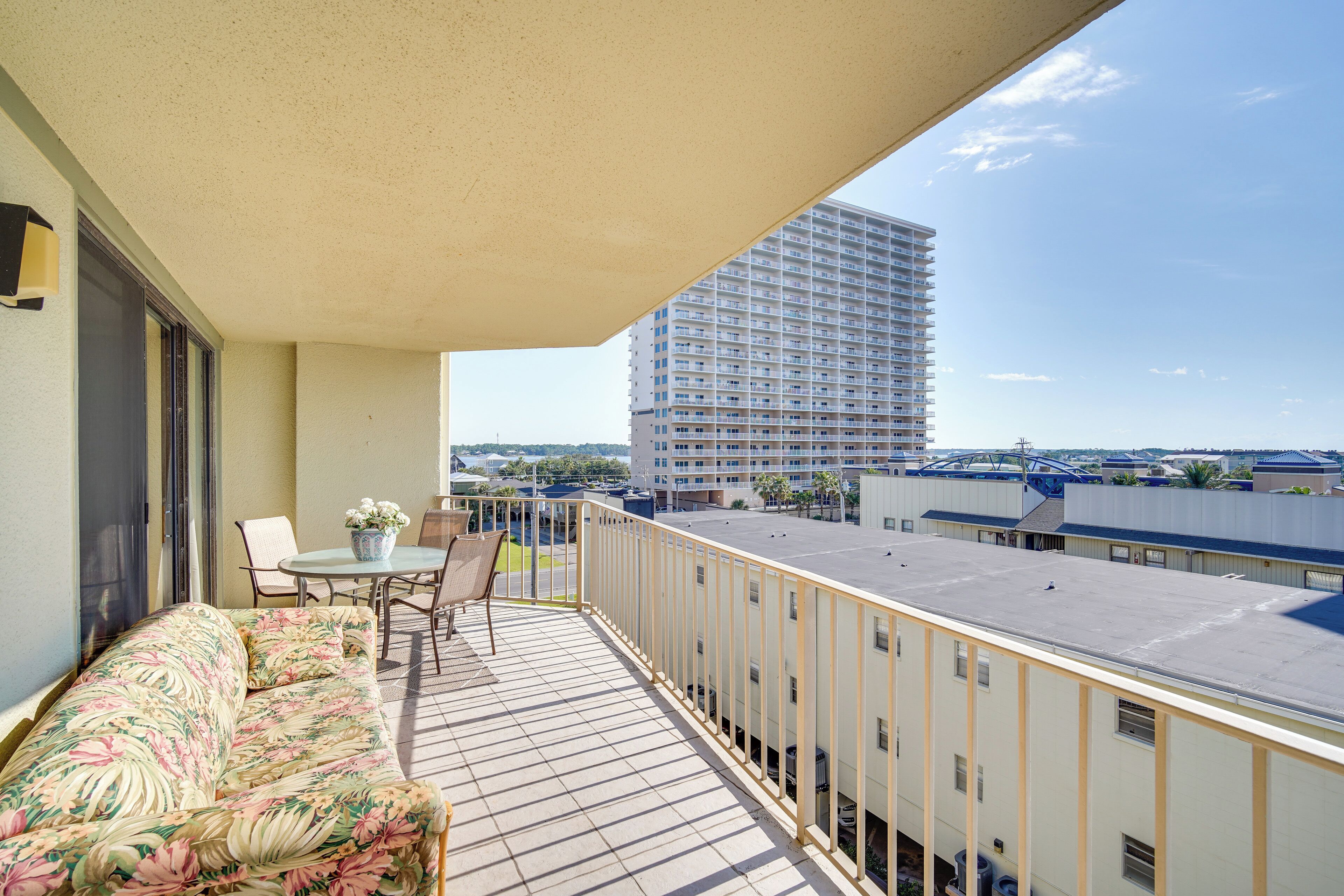 A balcony with a sofa and chairs, a table with a vase of flowers, and a view of a tall building.