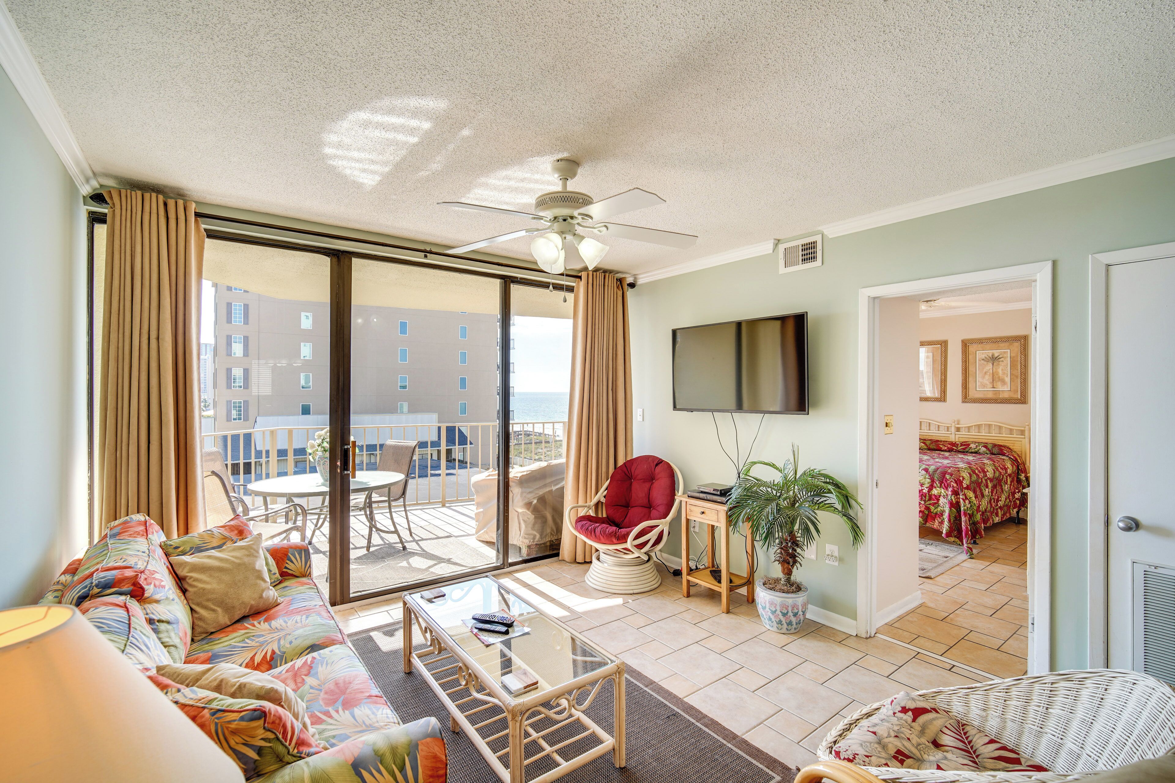 A spacious living area with a sofa, a glass coffee table, a red chair, and a television.