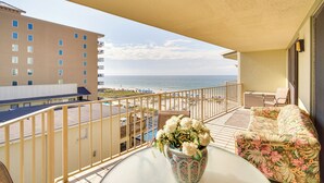 Ein Balkon mit Blick auf Strand und Meer, eine Blumenvase und ein Sofa.