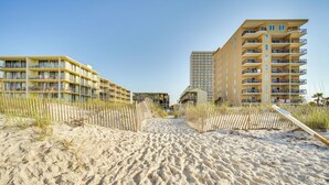 Ein Hotel direkt am Strand mit mehreren Balkonen, ein Sandstrand im Vordergrund und ein klarer Himmel.
