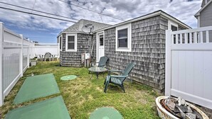 Une cour arrière avec une maison, une clôture blanche, une antenne parabolique et du mobilier d’extérieur.
