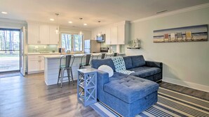 A modern kitchen with white cabinets, a dining area with a bar stool, and a living room with a blue sectional sofa.