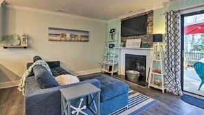A living room with a grey sectional sofa, a fireplace, a TV mounted on a stone wall, and a balcony with a red umbrella.
