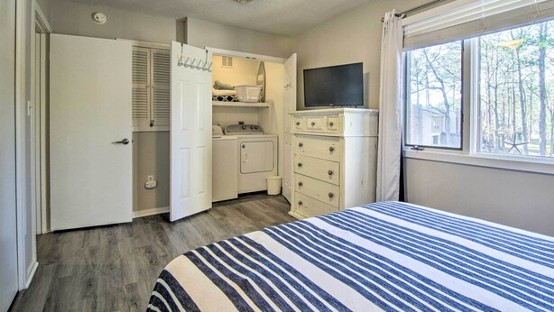 A bedroom with a bed, a ceiling fan, a TV, a window with a view of trees, and a closet with a hanging rack.