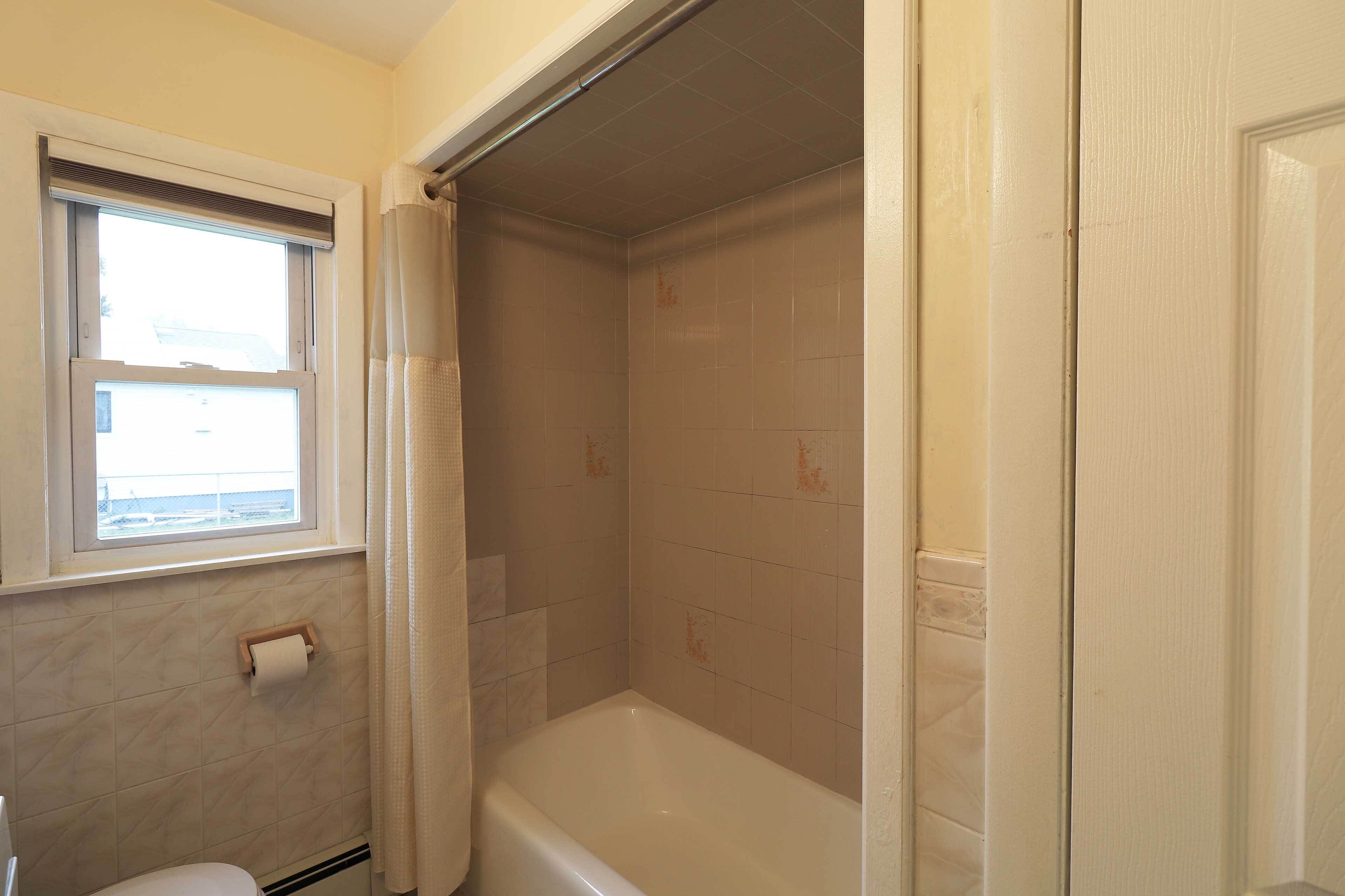 A bathroom with a bathtub, a toilet, a window, and a shower curtain.