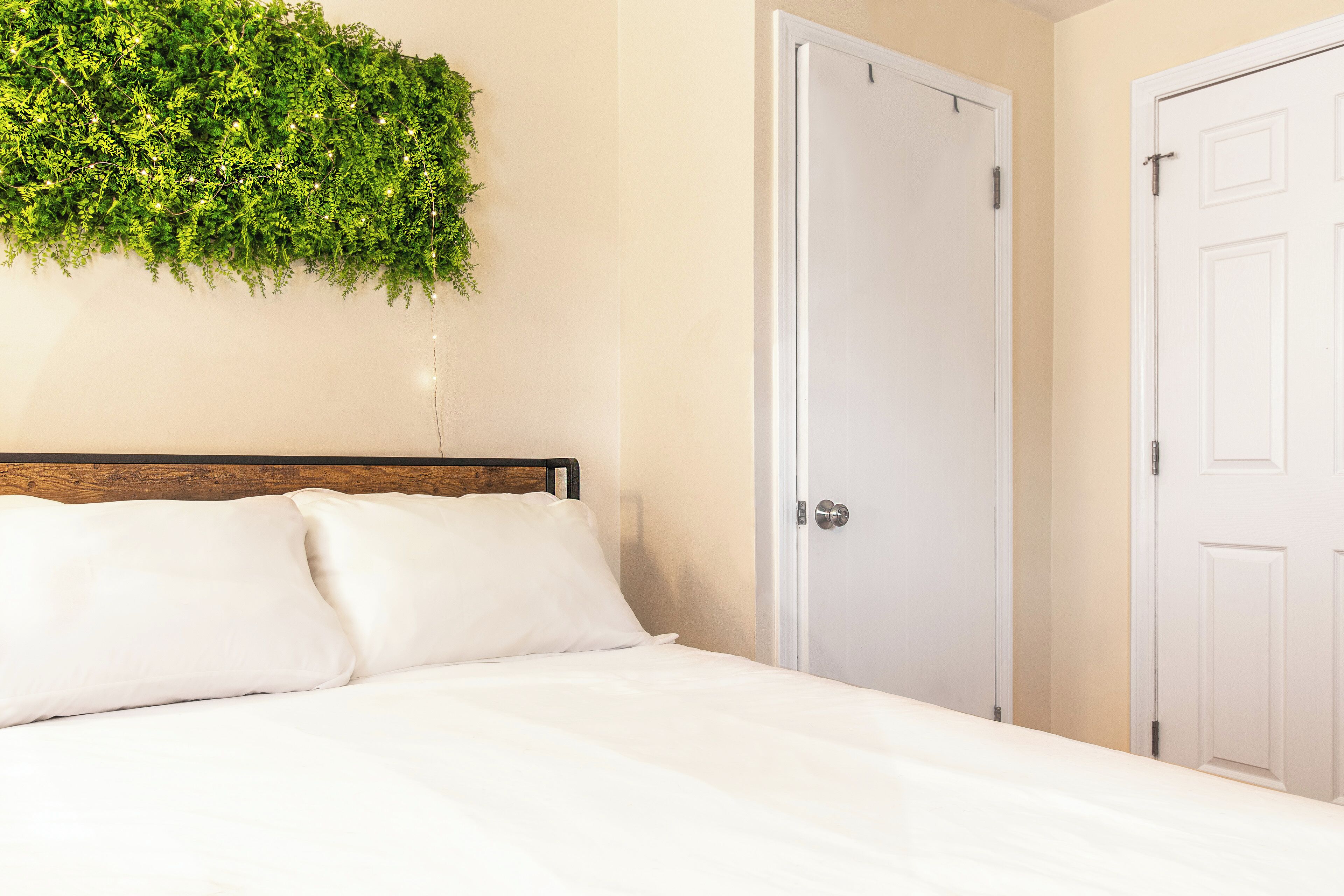 A bedroom with a bed, white pillows, a wooden headboard, a white door, and a green wall hanging.