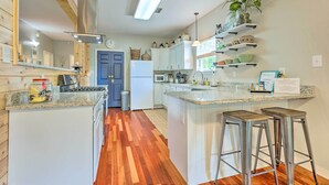 A modern kitchen with white cabinetry, a central island, and bar stools. - Bayou La Batre Stilted House on Snake Bayou! (Bayou La Batre)