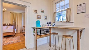 A bedroom with a bed, a wooden table with a microwave, and two stools. - Renovated Historic Home w/ Yard: 2 Mi to Dtwn (Mobile)