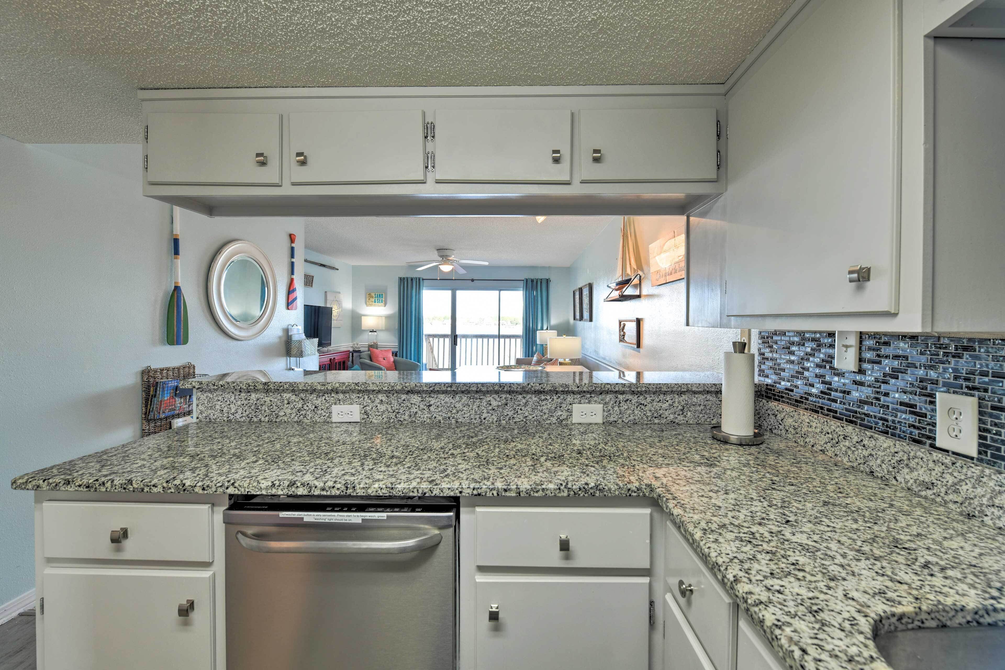 A kitchen with granite countertops, white cabinetry, a dishwasher, and a view to the living area.
