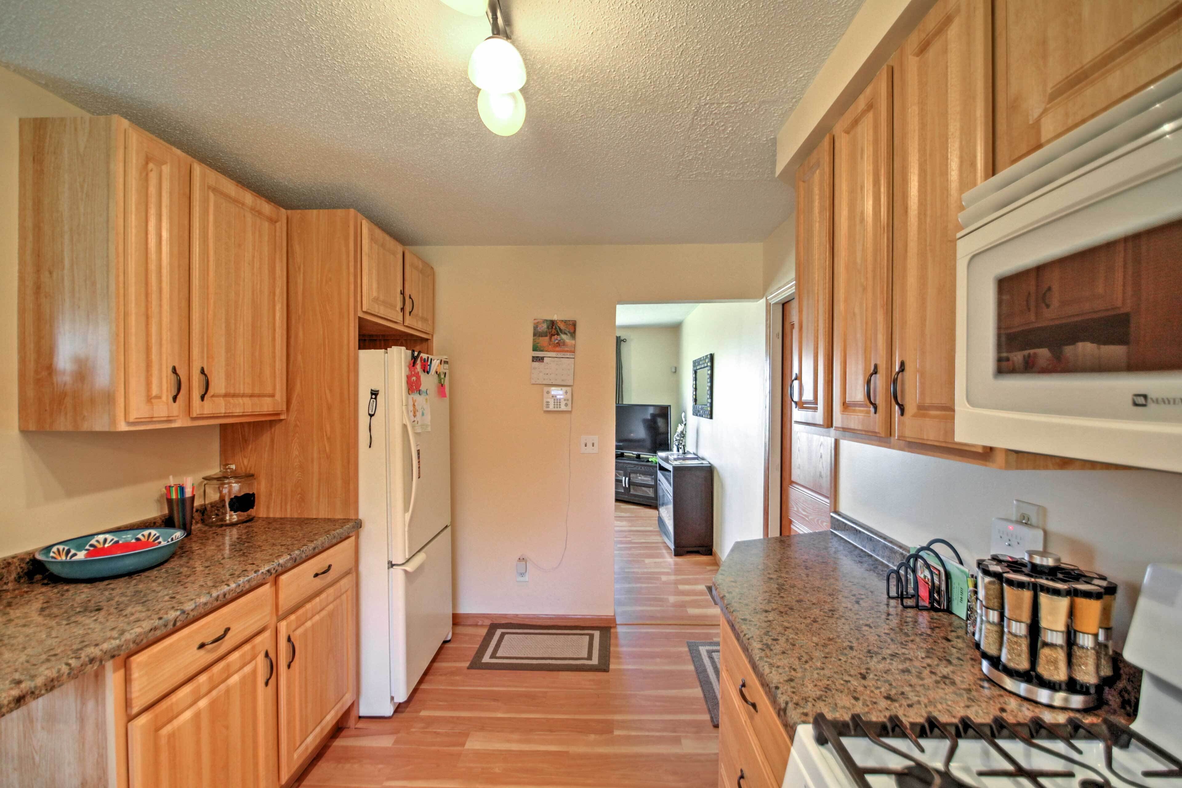 A kitchen with wooden cabinets, a granite countertop, a refrigerator, a stove, and a microwave.
