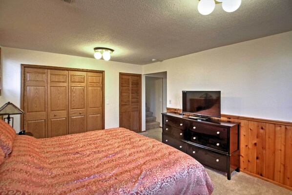 A bedroom with a large bed, wooden wardrobe, a dresser with drawers, a television, and a ceiling light fixture.