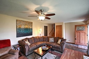 A living room with a sectional sofa, a coffee table, a ceiling fan, and a painting on the wall.