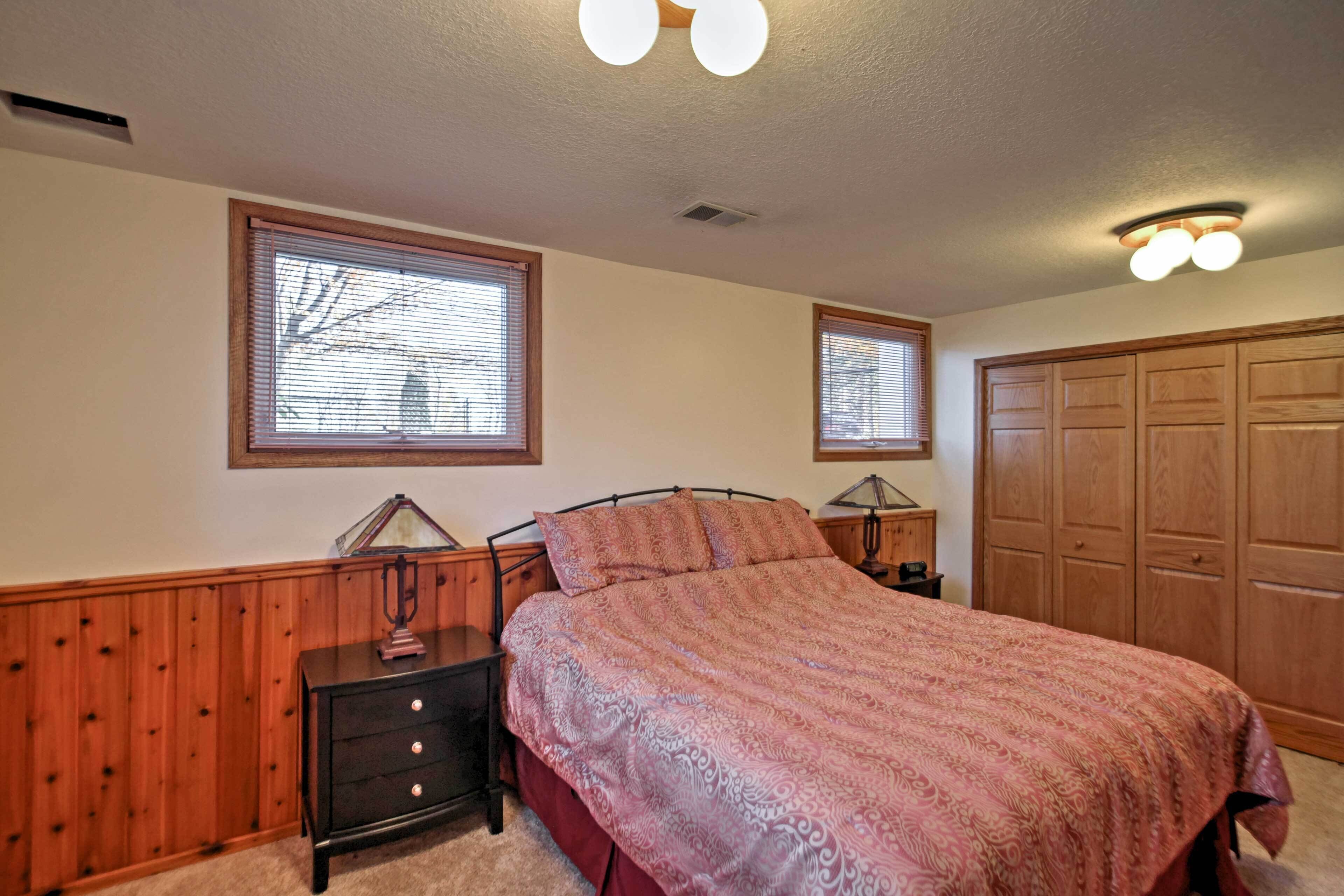 Une chambre à coucher comprenant un lit, une armoire en bois, deux tables de chevet et une fenêtre avec des stores.