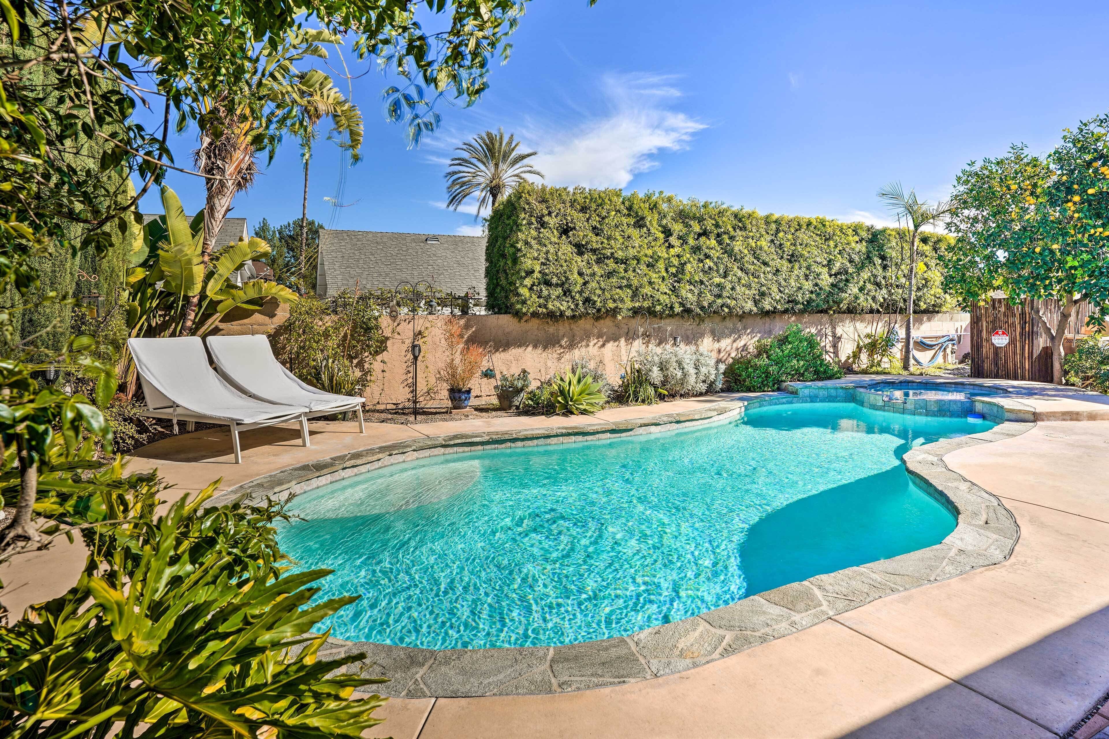 A swimming pool with two lounge chairs, surrounded by lush greenery and a stone wall.