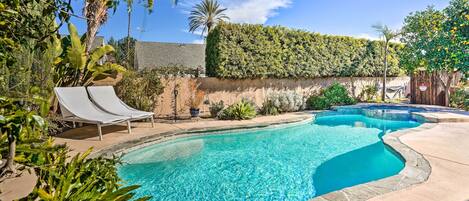 A swimming pool with two lounge chairs, surrounded by lush greenery and a stone wall.