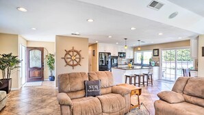 A spacious living room with a large brown leather sofa, a wooden coffee table, and a rug. There is a kitchen area visible in the background with white cabinets and a dining area with a wooden table and chairs. - Deluxe Laguna Hills Home w/ Outdoor Oasis! (Laguna Hills)