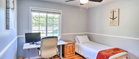 A bedroom with a single bed, a desk with a computer, a chair, a wooden cabinet, and a ceiling fan.