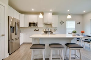A modern kitchen with white cabinets, stainless steel appliances, and a central island with bar stools. - Covered Patio, Grill & Hammock: Frankford Home! (Selbyville)