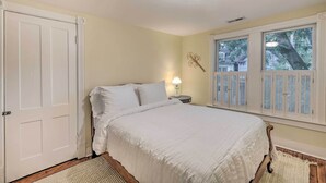 A bedroom with a bed, a nightstand, a lamp, a window with shutters, and a door.