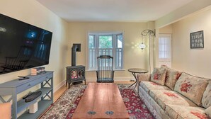A living room with a flat-screen TV, a wooden coffee table, a sofa, a chair, a fireplace, and a window with blinds.