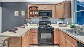 A kitchen with wooden cabinets, a black stove, a microwave, and a sink.