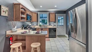 A modern kitchen with wooden cabinets, a stainless steel refrigerator, and a central island with stools.