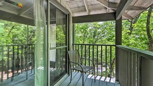 A covered outdoor area with a metal chair, glass sliding doors, and a view of a wooded area.