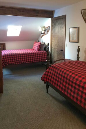 A room with two beds, each with a checkered bedspread, a wooden chair, a lamp, and a door. - Stowe Vacation Rental w/ Deck & Mountain Views! (Stowe)